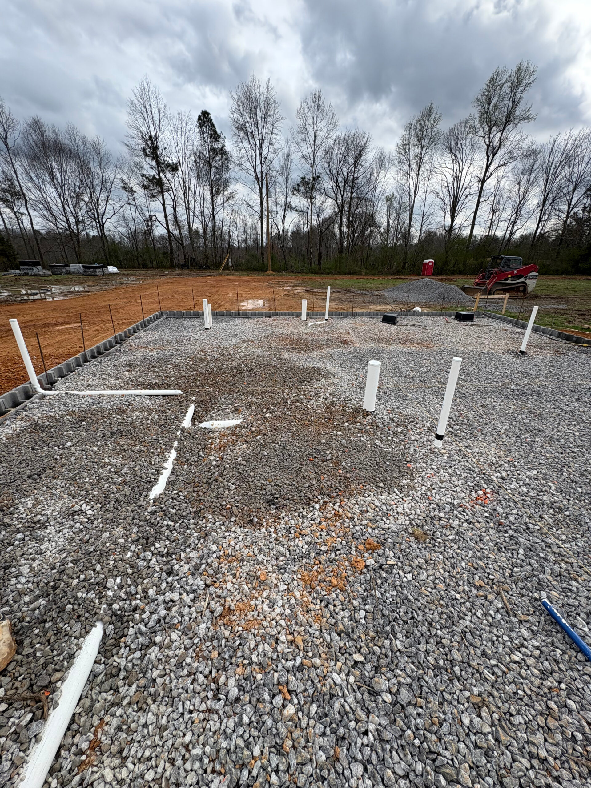 Plumbing pipes and risers prepared within a gravel-filled building foundation